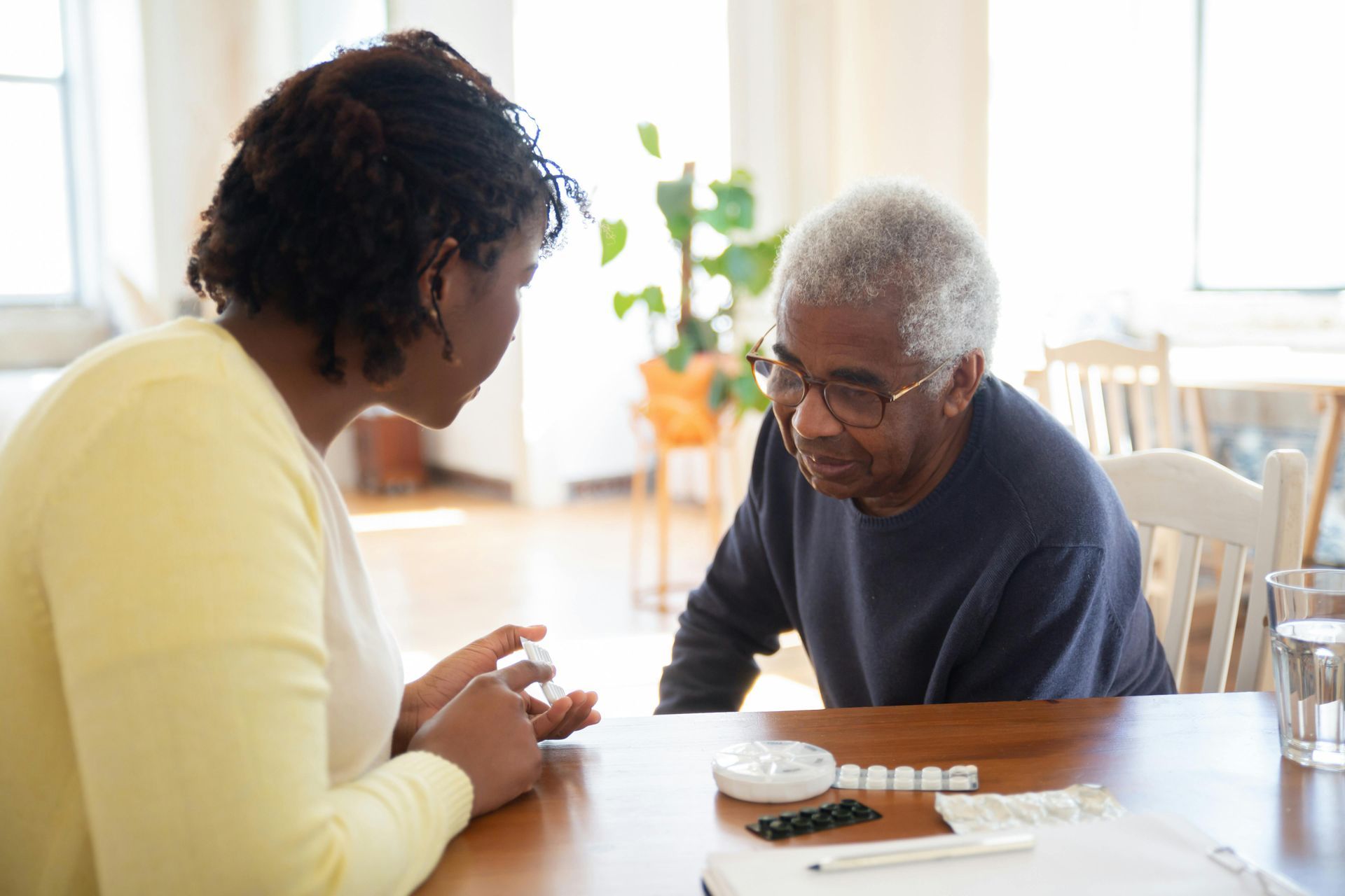 Woman speaking to senior man at table with medication.