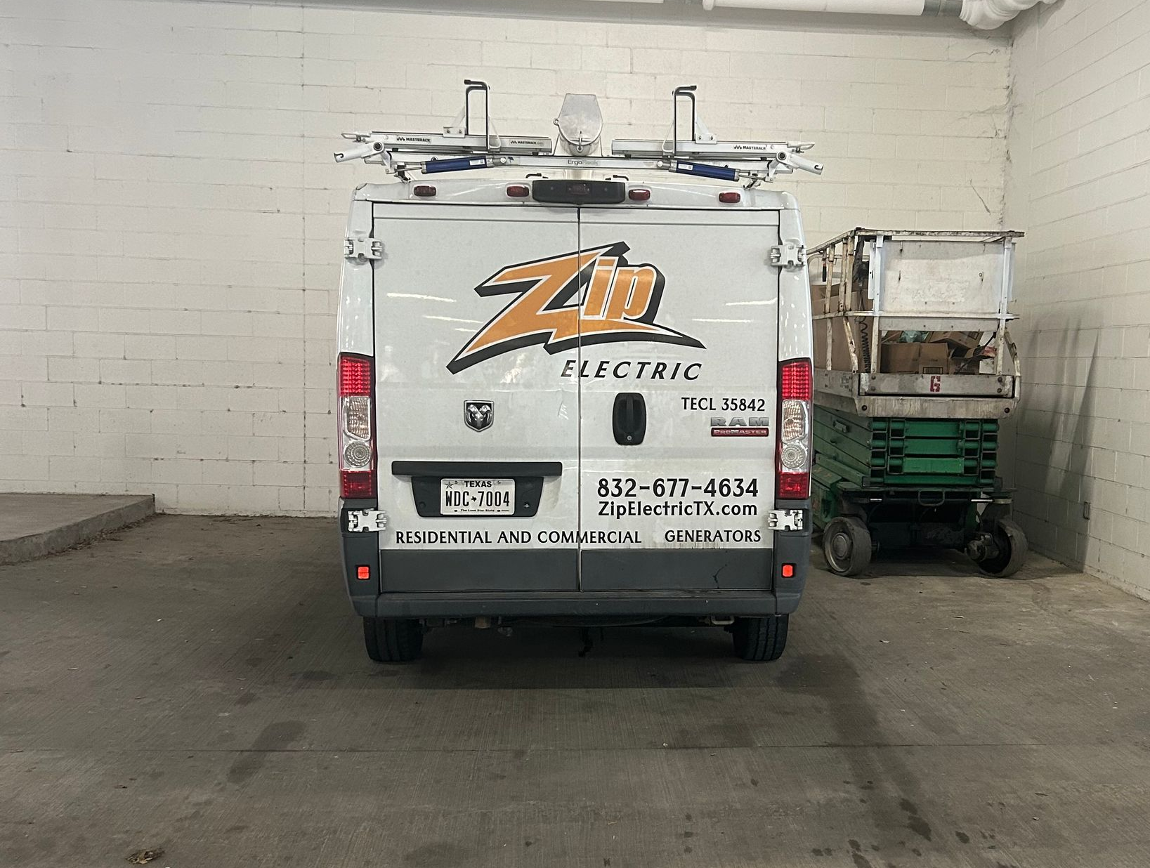 White ZM Electric van with ladder rack parked next to a lift in a garage.