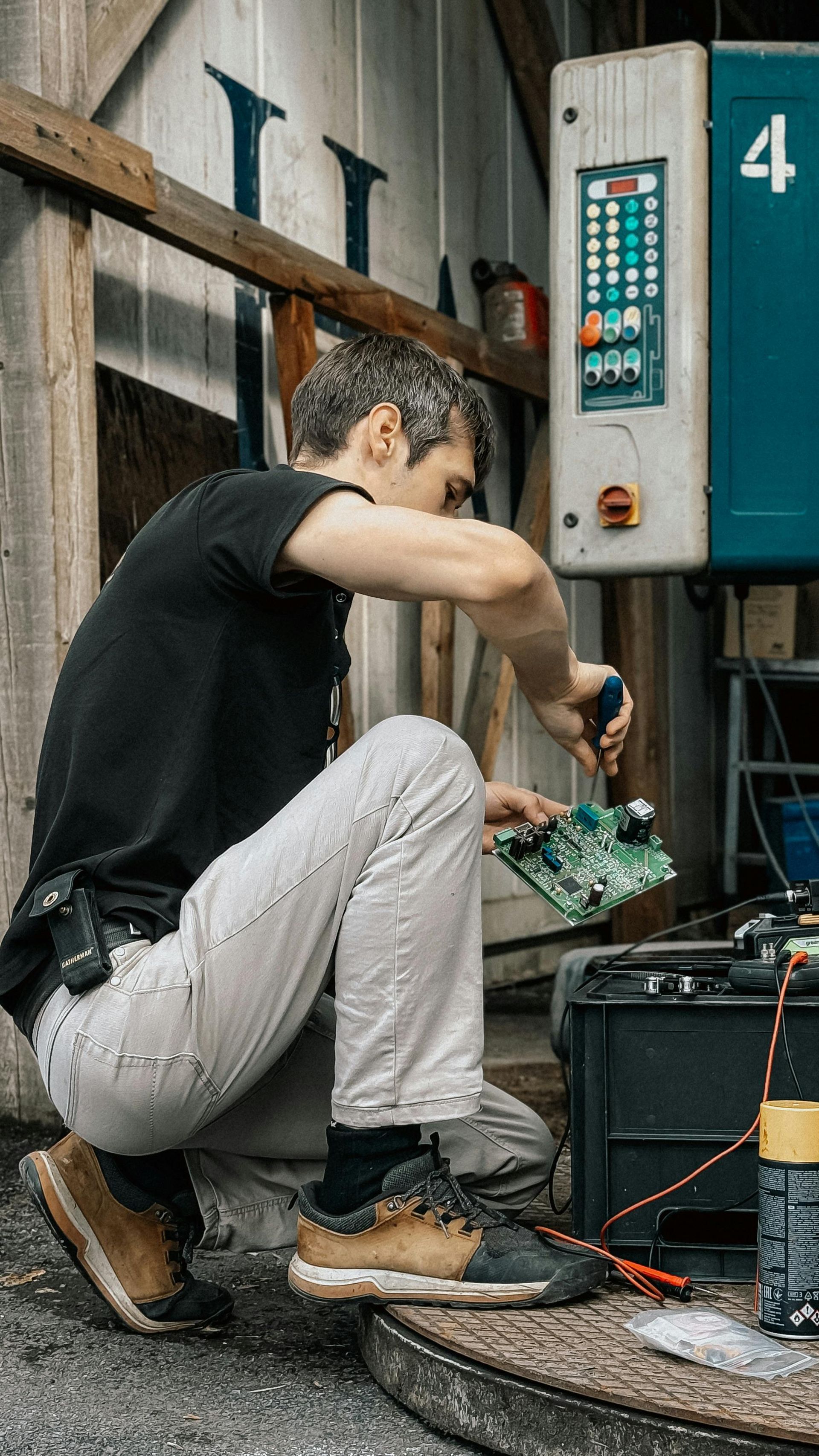 Man crouches, using a screwdriver on a circuit board near a control panel with the number 