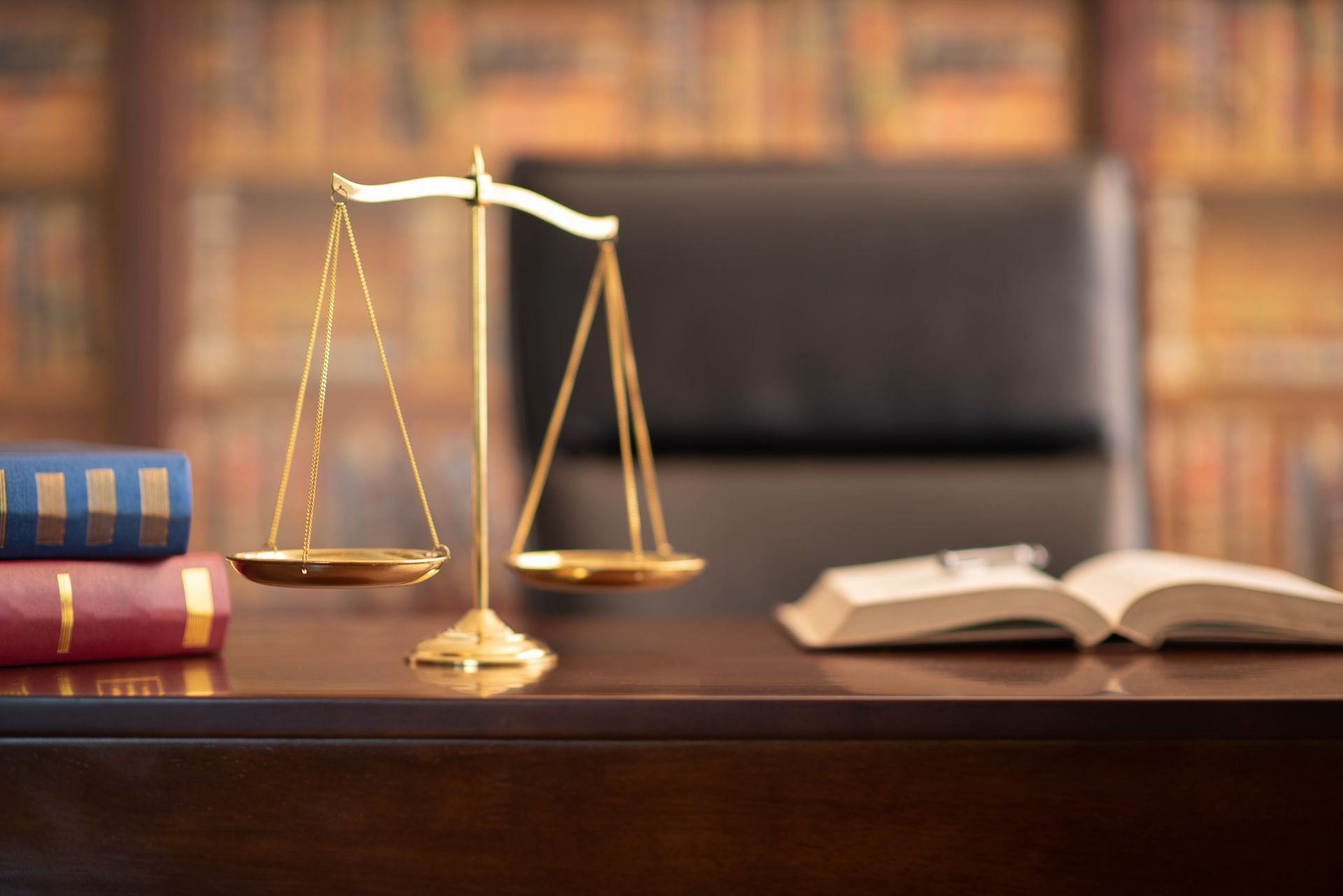 A scale of justice is sitting on a wooden desk next to a stack of books.