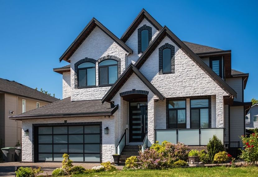 Large white and gray two-story house with dark roof, garage, and front lawn under a clear blue sky