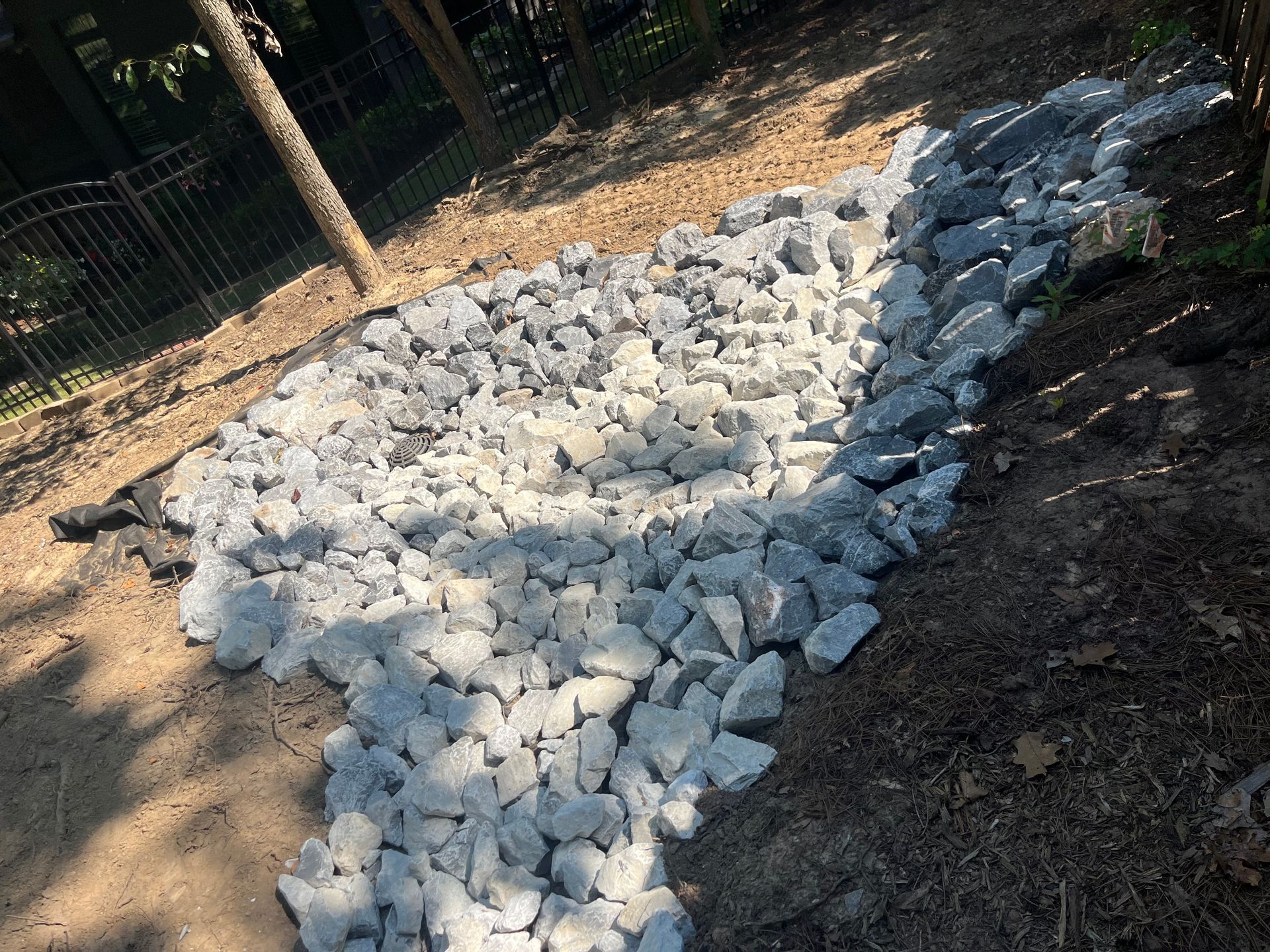 White rocks arranged in a rough heart shape on dirt ground near a fence, in sunlight