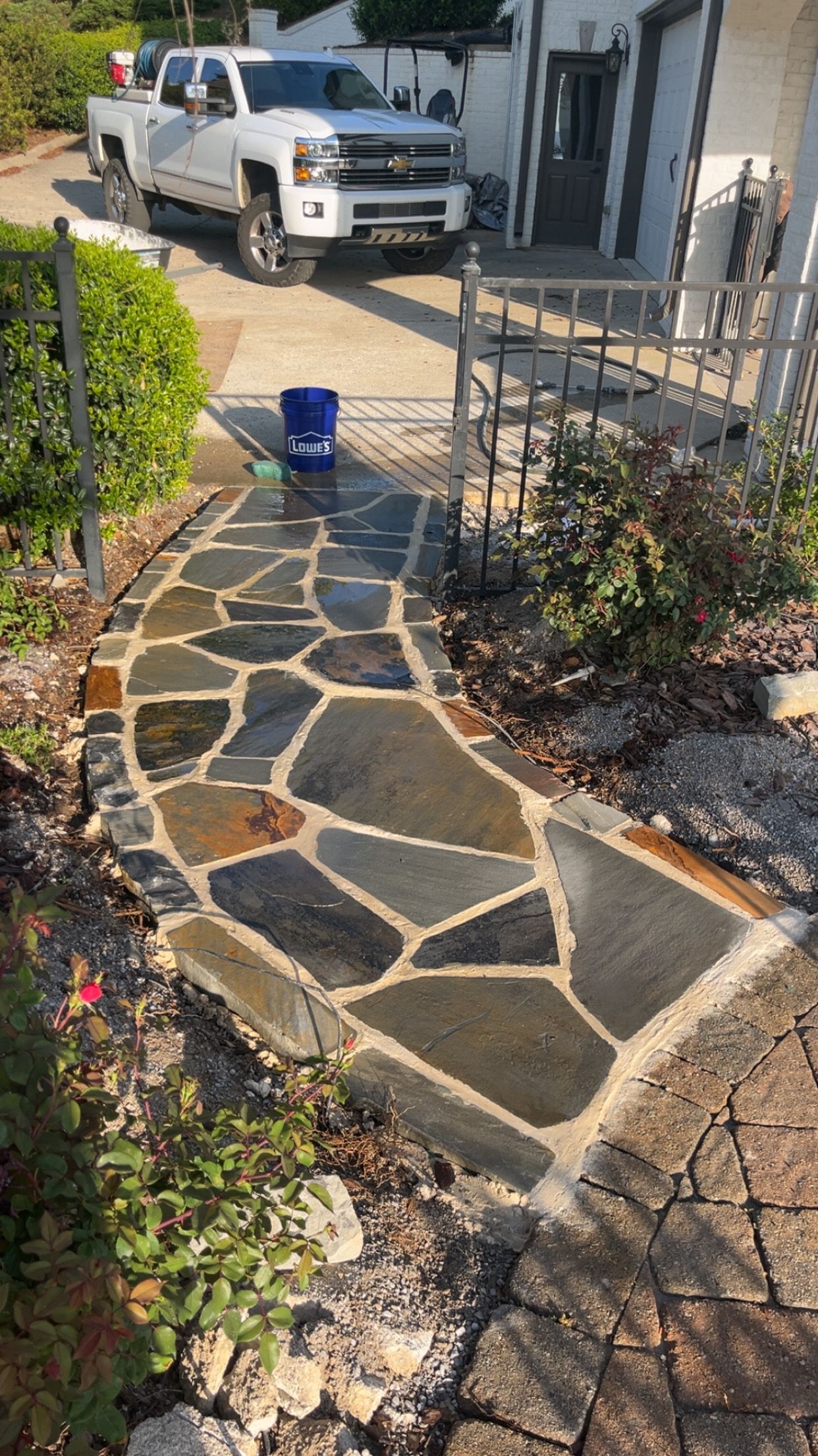 Stone walkway under construction with irregular pavers, a blue bucket, and a white truck parked nearby.