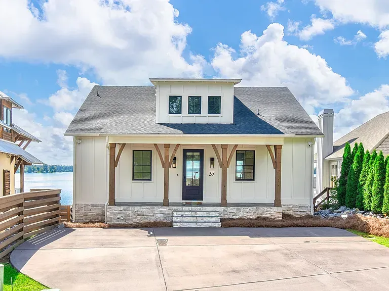 Small white beach house with blue-gray roof, front porch, and driveway by the water
