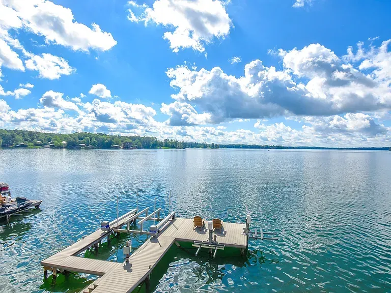 Dock with two people on a calm blue lake under a bright, cloudy sky