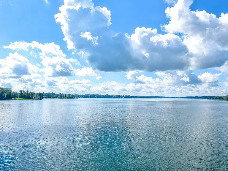 Calm blue lake under a bright sky with scattered white clouds and a distant tree-lined shore