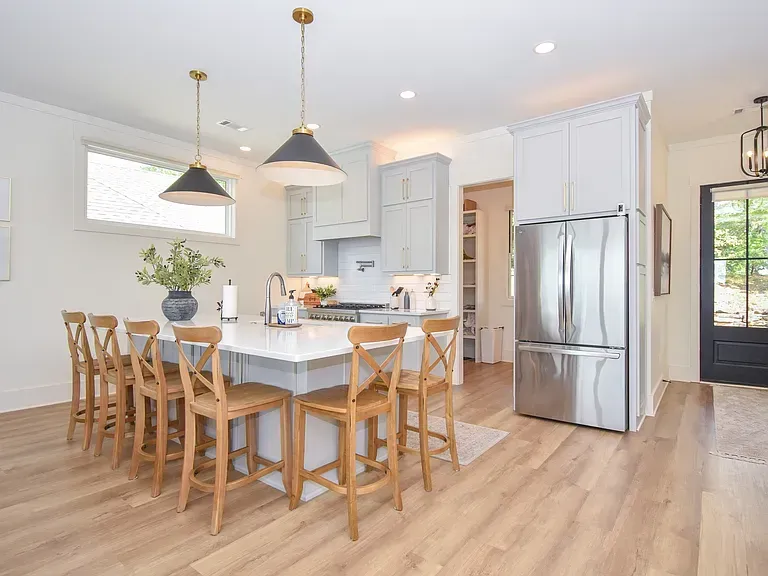 Bright modern kitchen with white cabinets, wood floors, island, bar stools, and stainless steel refrigerator