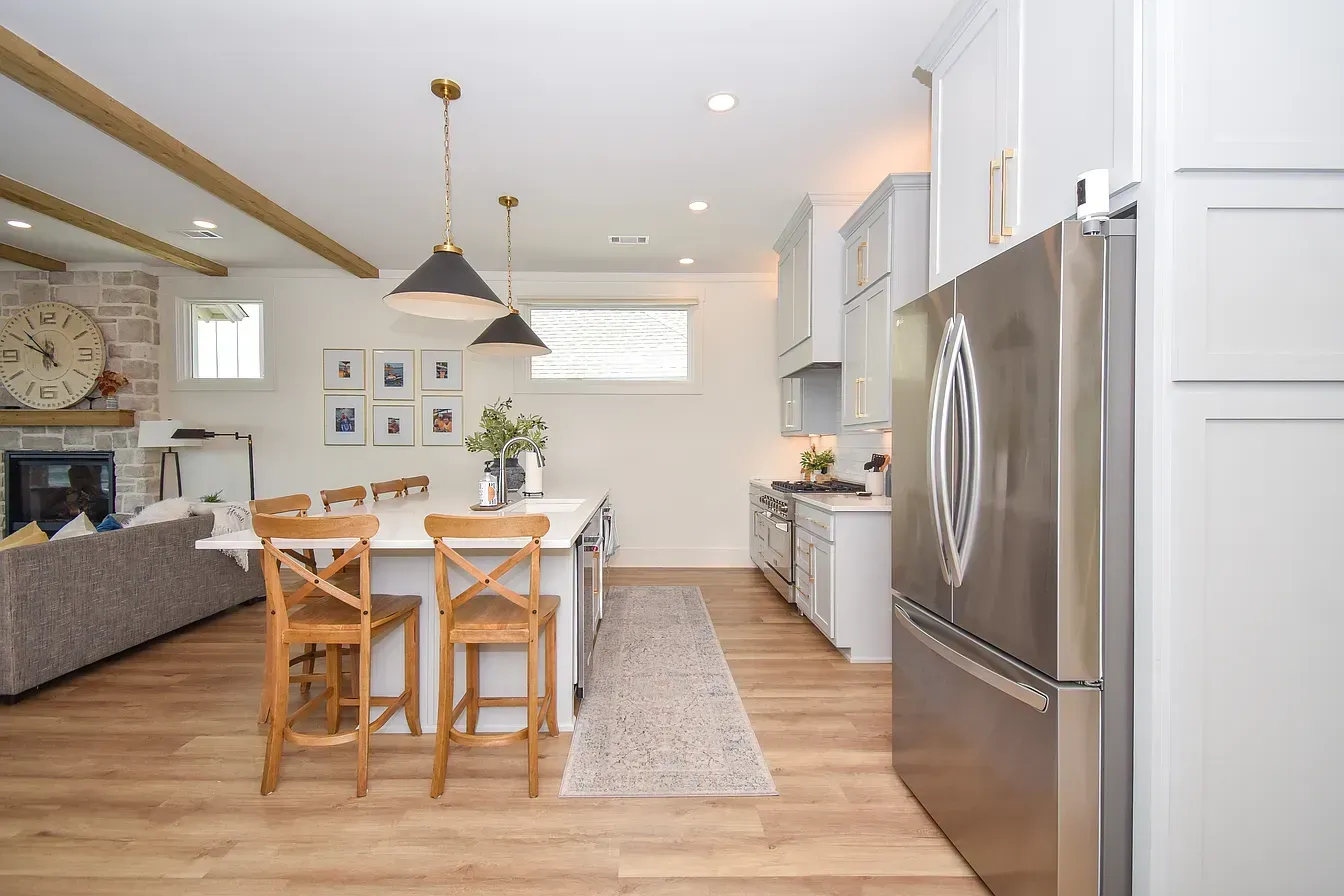 Bright kitchen with wooden dining table, stainless steel fridge, white cabinets, and pendant lights