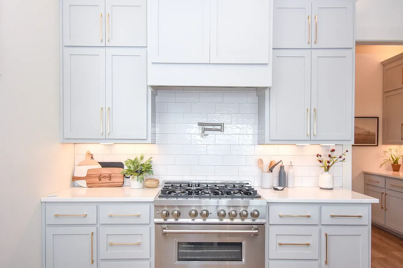 Bright white kitchen with stainless stove, cabinets, subway tile backsplash, and small plants on the counter