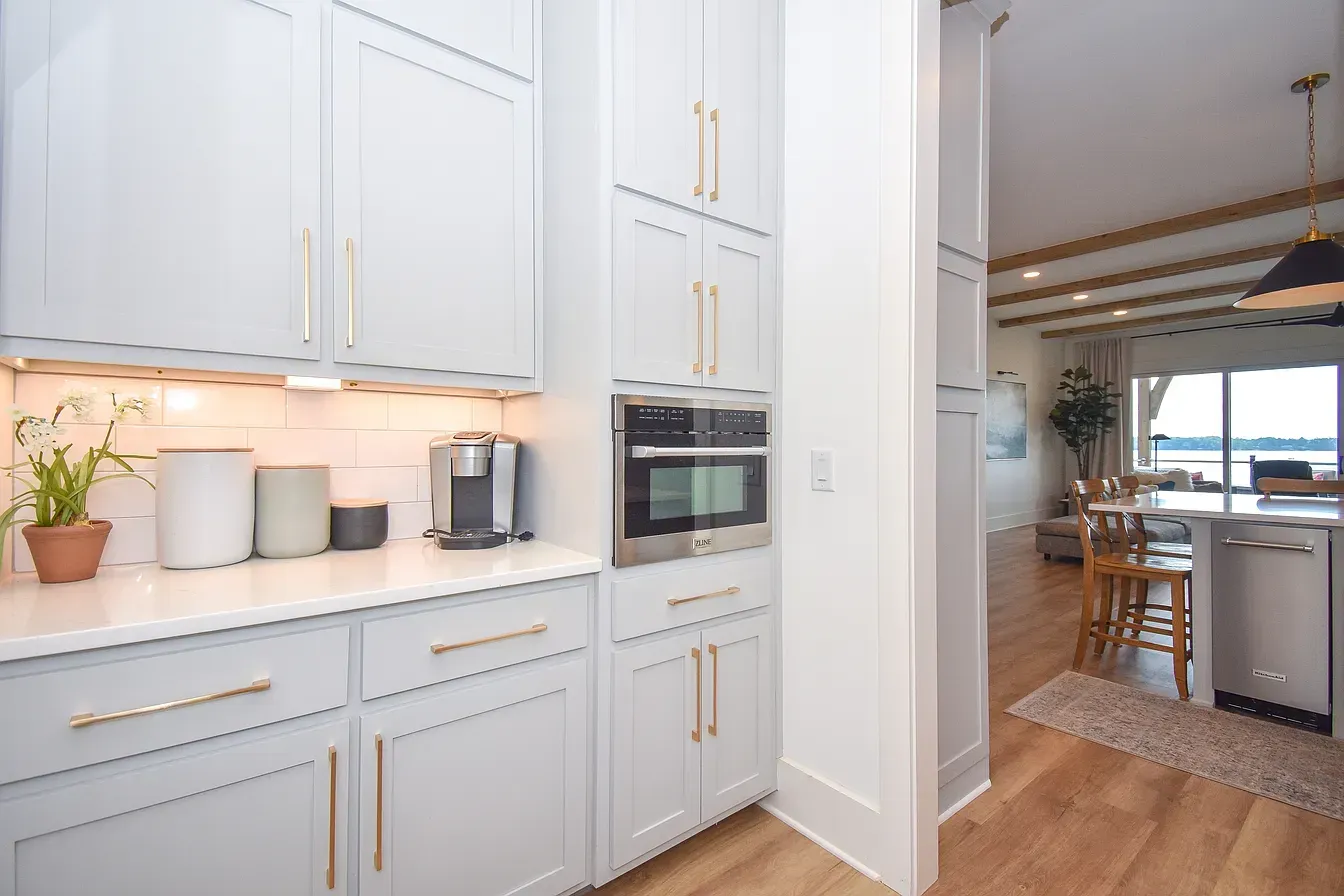 Bright white kitchen with built-in oven, countertop plants, and view into a dining area.