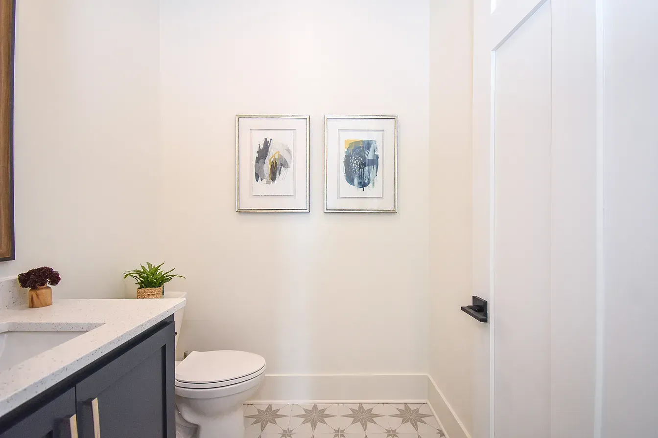 Bright bathroom with a vanity, toilet, and two framed prints on white walls