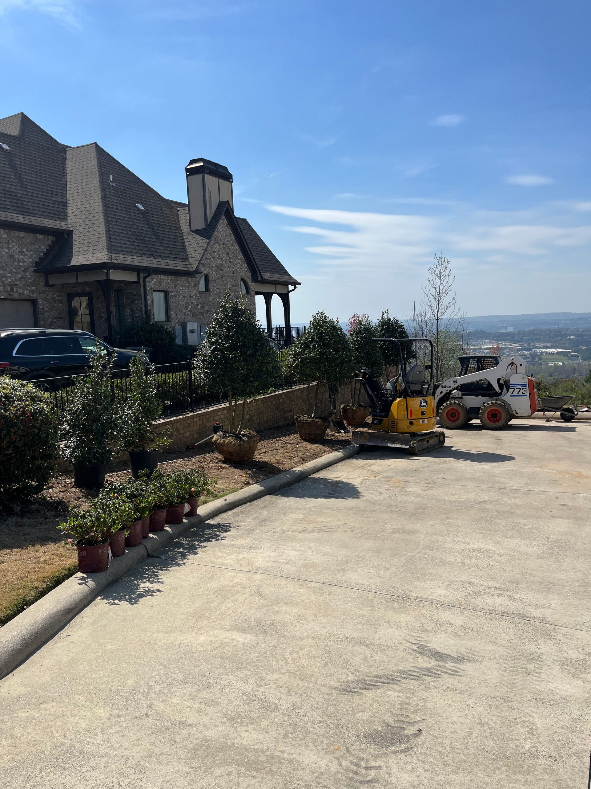 Driveway beside a stone house on a hill with landscaping and a distant city view