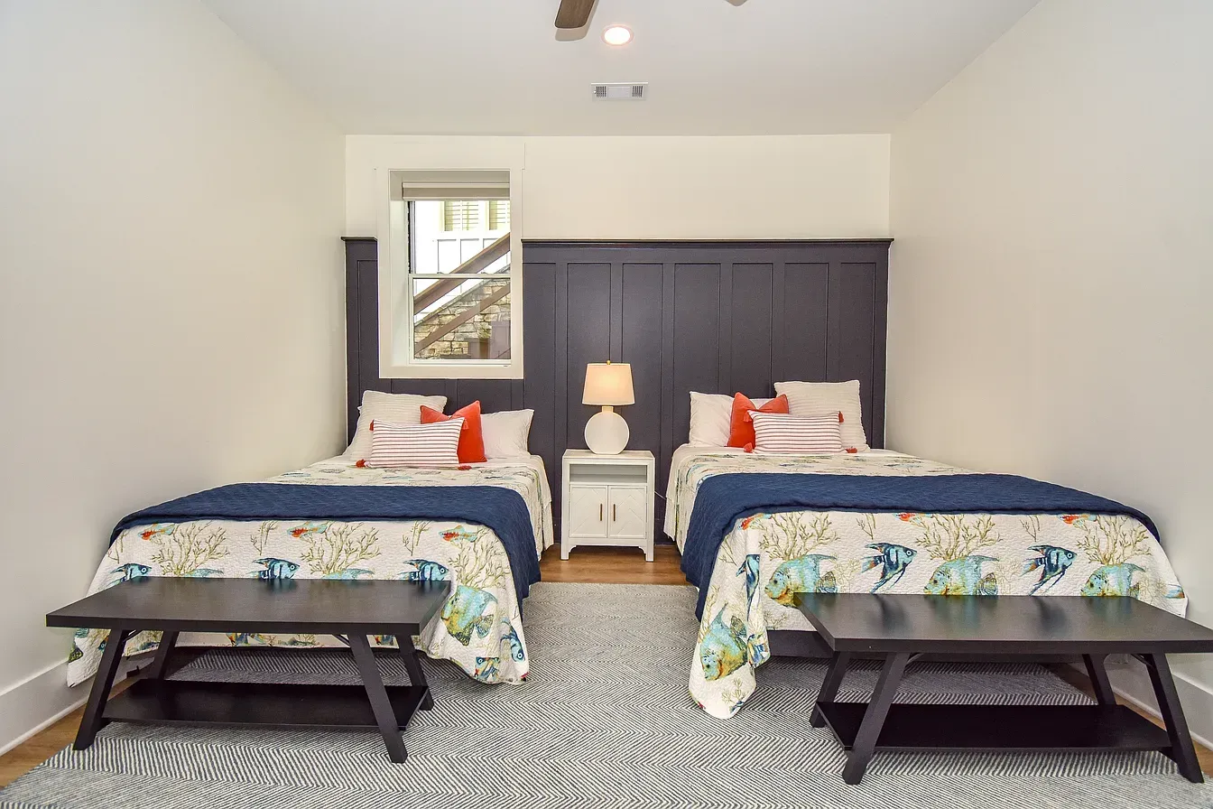 Bright bedroom with two twin beds, blue bedding, bedside lamp, and dark wood benches on a patterned rug