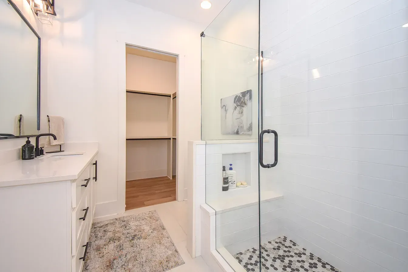 Bright bathroom with glass shower door, white vanity, and doorway to a closet.