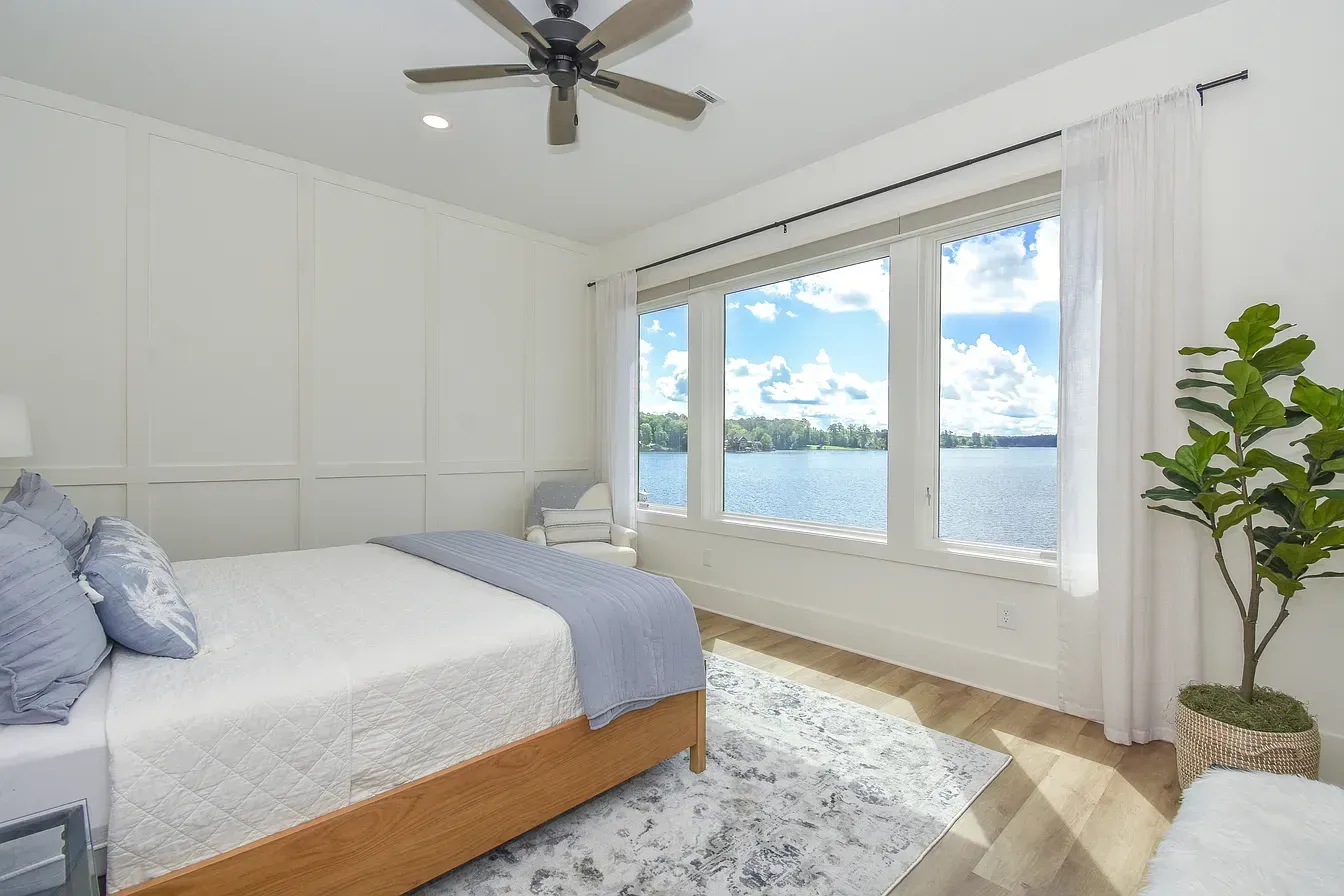 Bright bedroom with white bed, large windows, ocean view, and a potted plant