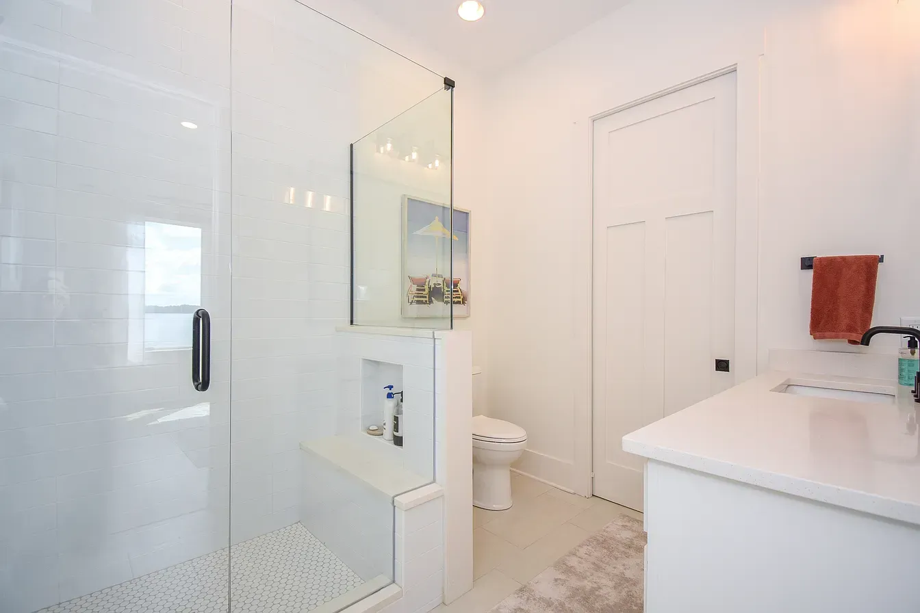 Bright white bathroom with glass shower, vanity sink, and closed door