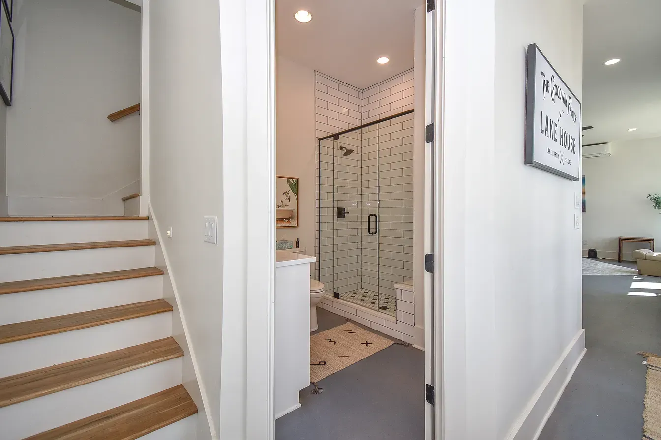 Bright hallway with wooden stairs, a tiled shower, and a view into a living room