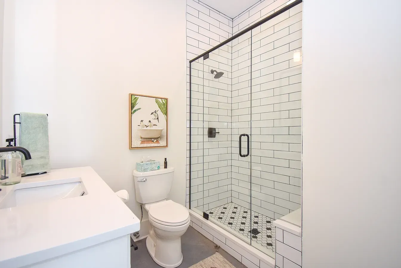 Bright white bathroom with sink, toilet, and glass shower enclosure with patterned tile.