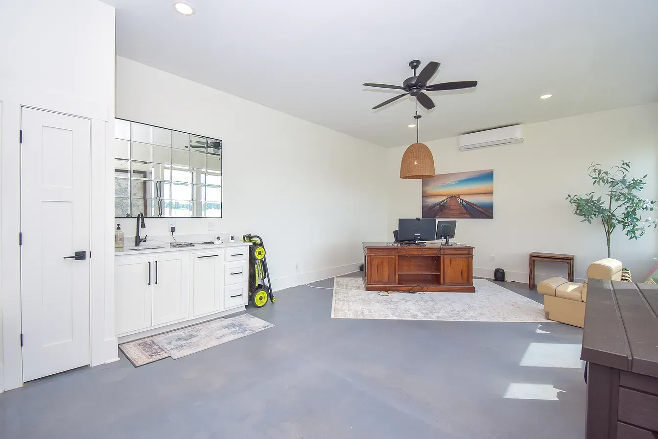 Bright living room with white walls, gray carpet, ceiling fan, wooden coffee table, and wall art.
