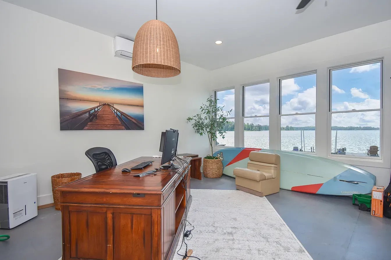 Bright home office with wooden desk, black chairs, ocean photo, large windows, and a cozy reading nook.