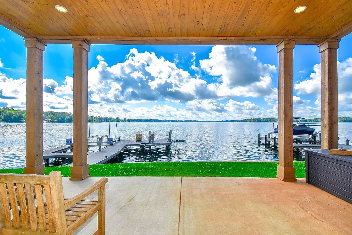 Covered lakeside patio with wooden posts, dock, and bright blue sky over calm water
