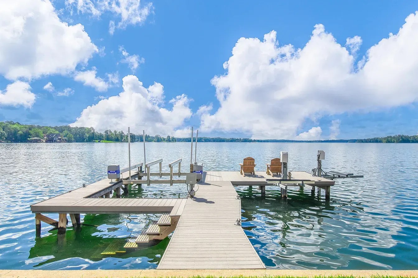 Wooden dock extending into a calm lake under a bright blue sky with large white clouds