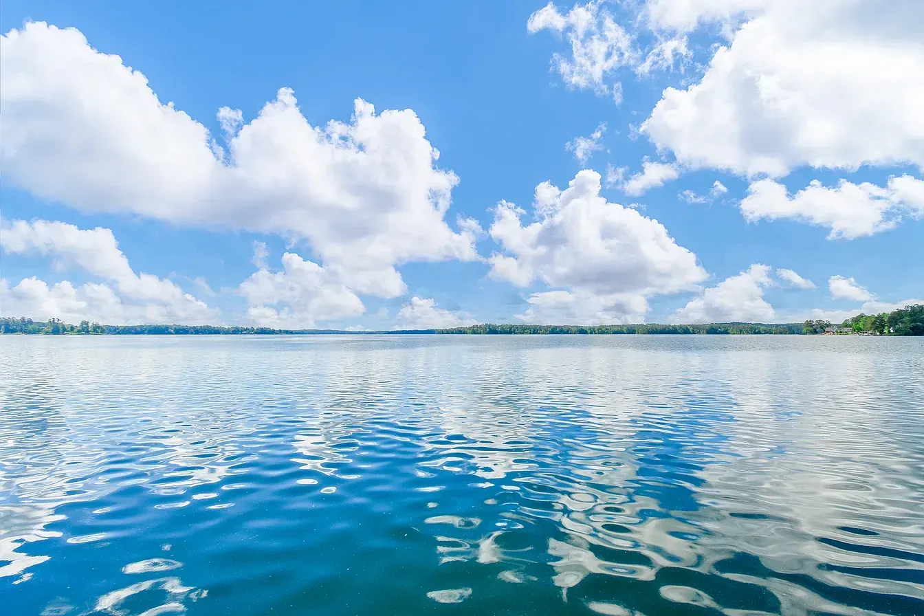 Calm blue ocean under a bright sky with fluffy white clouds reflecting on the water
