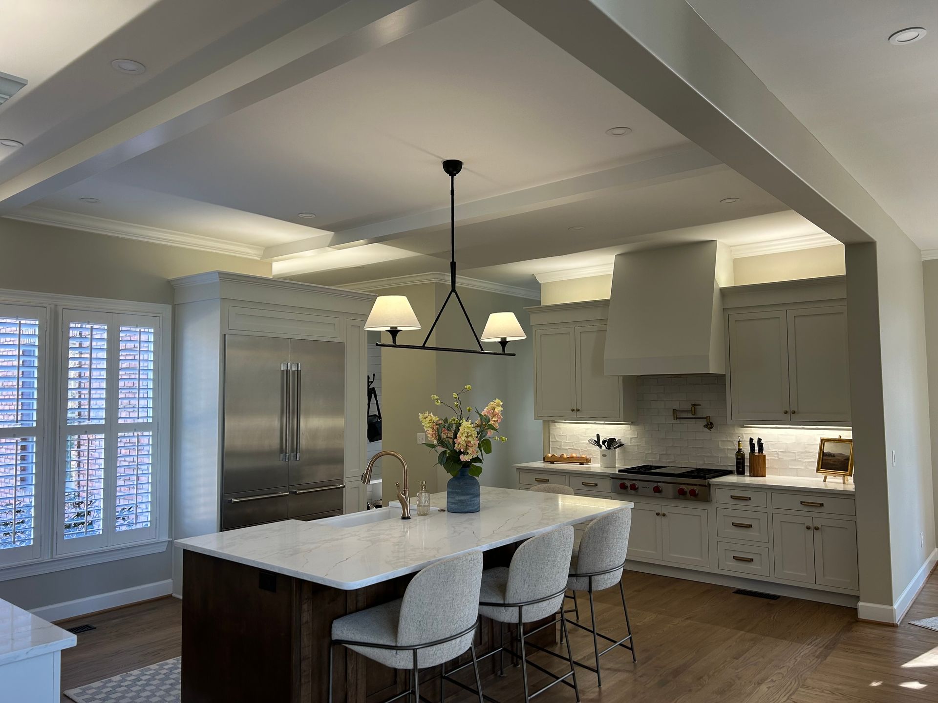 Modern kitchen with island, pendant lights, white cabinets, stainless fridge, and large windows