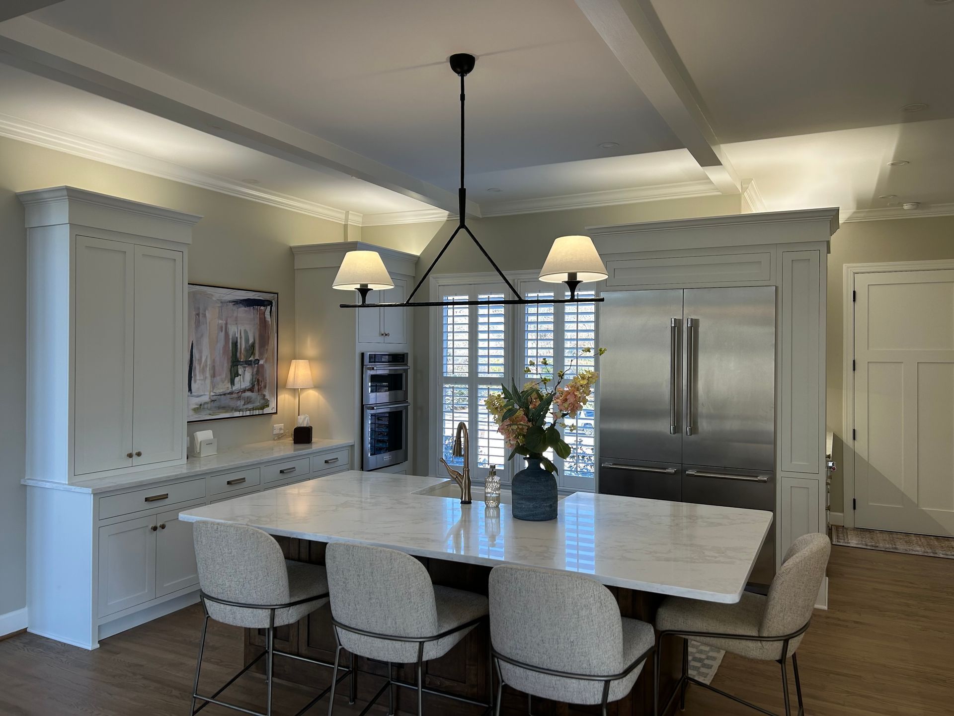 Modern kitchen with a large island, pendant lights, white cabinets, and stainless steel refrigerator