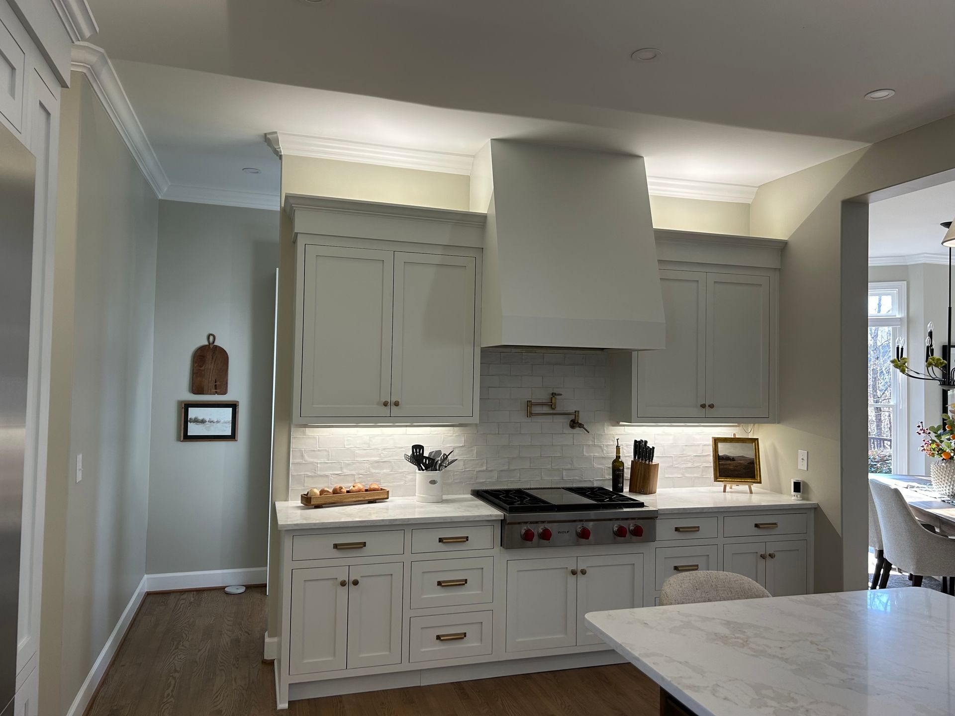 Modern white kitchen with large range hood, marble island, and bright windows