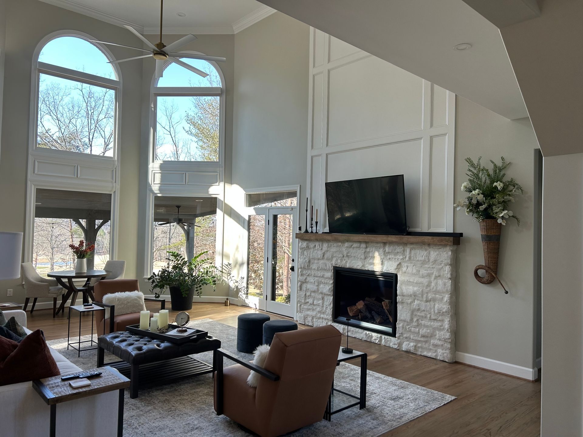 Bright living room with tall windows, fireplace, leather chair, and views of trees outside.