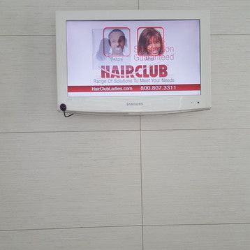A television is hanging on a white tiled wall.