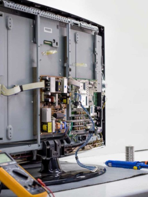 A computer monitor is being repaired with a multimeter