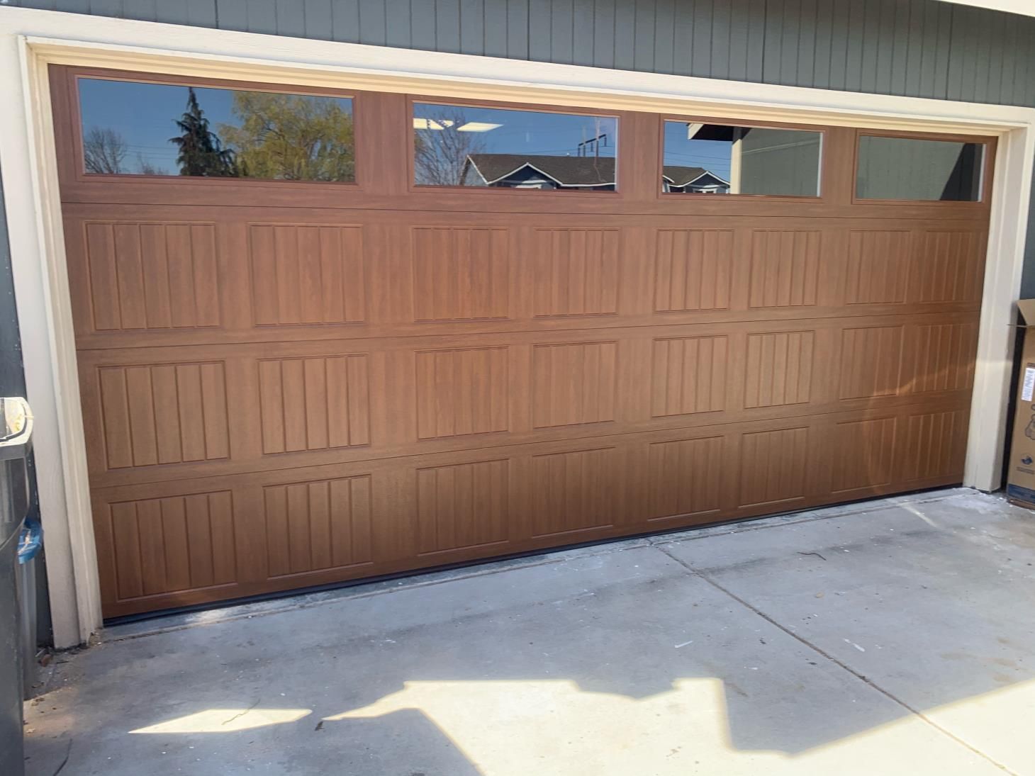 A brown garage door with a lot of windows is sitting in front of a house.