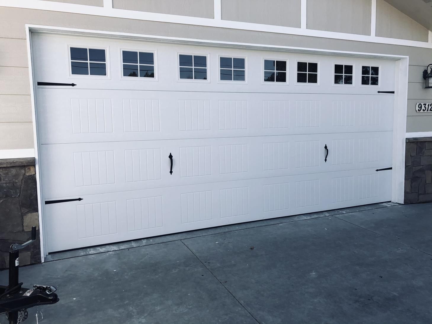 A white garage door with windows is sitting in front of a house.