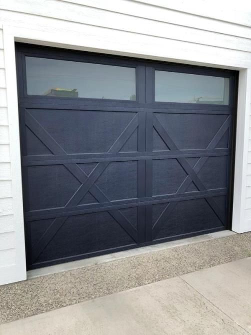 A black garage door with a glass window is on a white house.