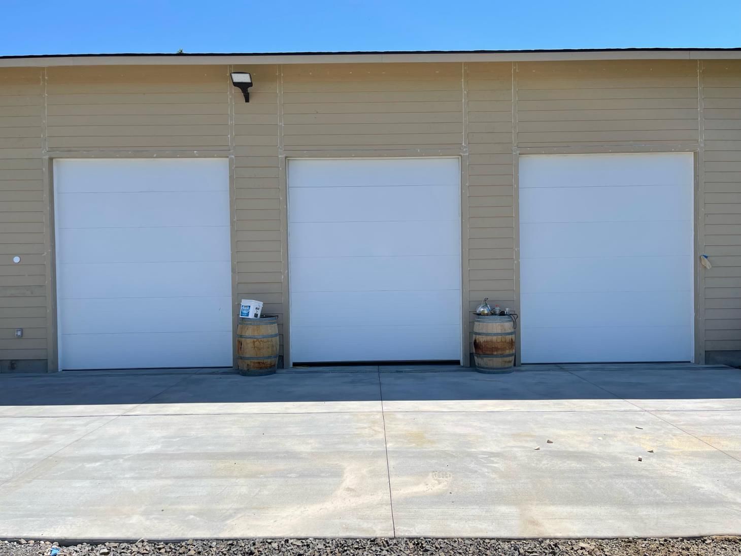 Three white garage doors with barrels in front of them