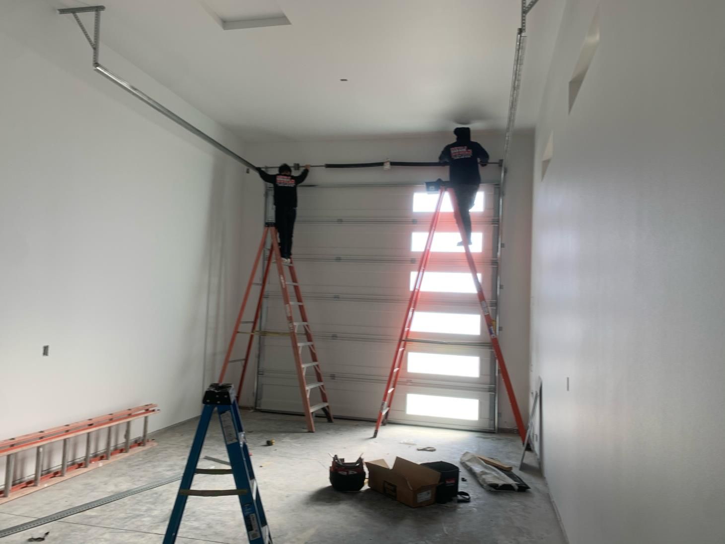 Two men are working on a garage door with ladders.