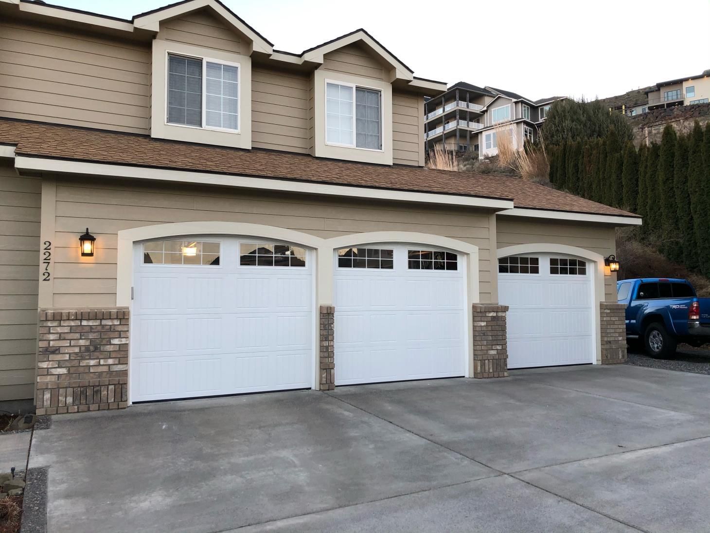 A house with three white garage doors and a blue truck parked in front of it.