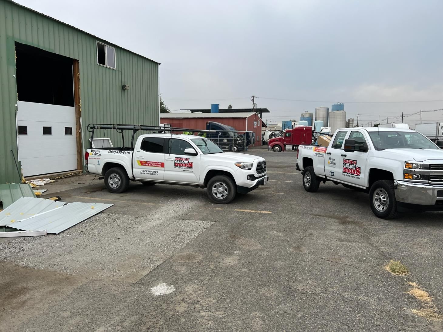 Two white trucks are parked in a parking lot in front of a building.