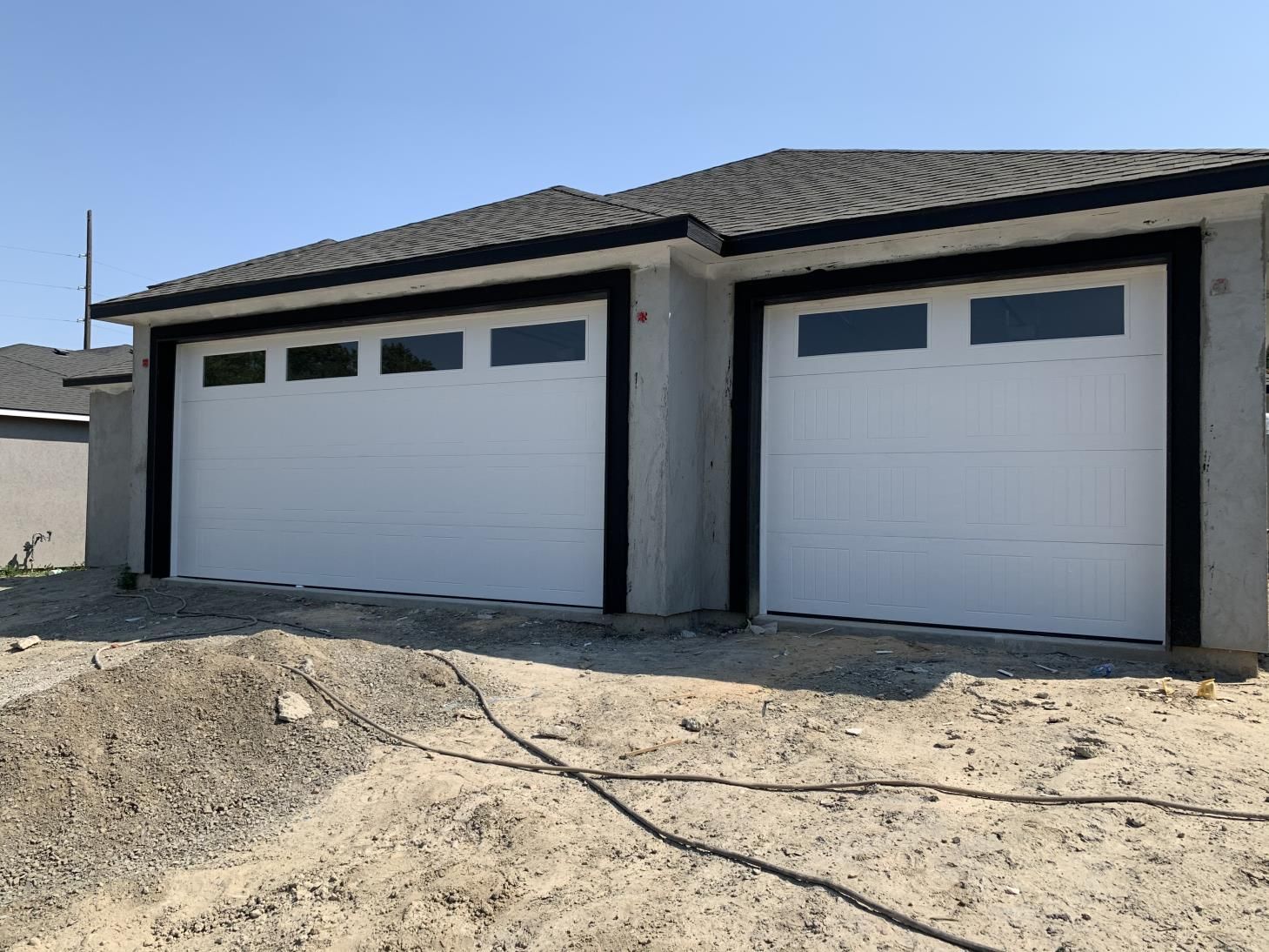 Two white garage doors are sitting next to each other in front of a house.