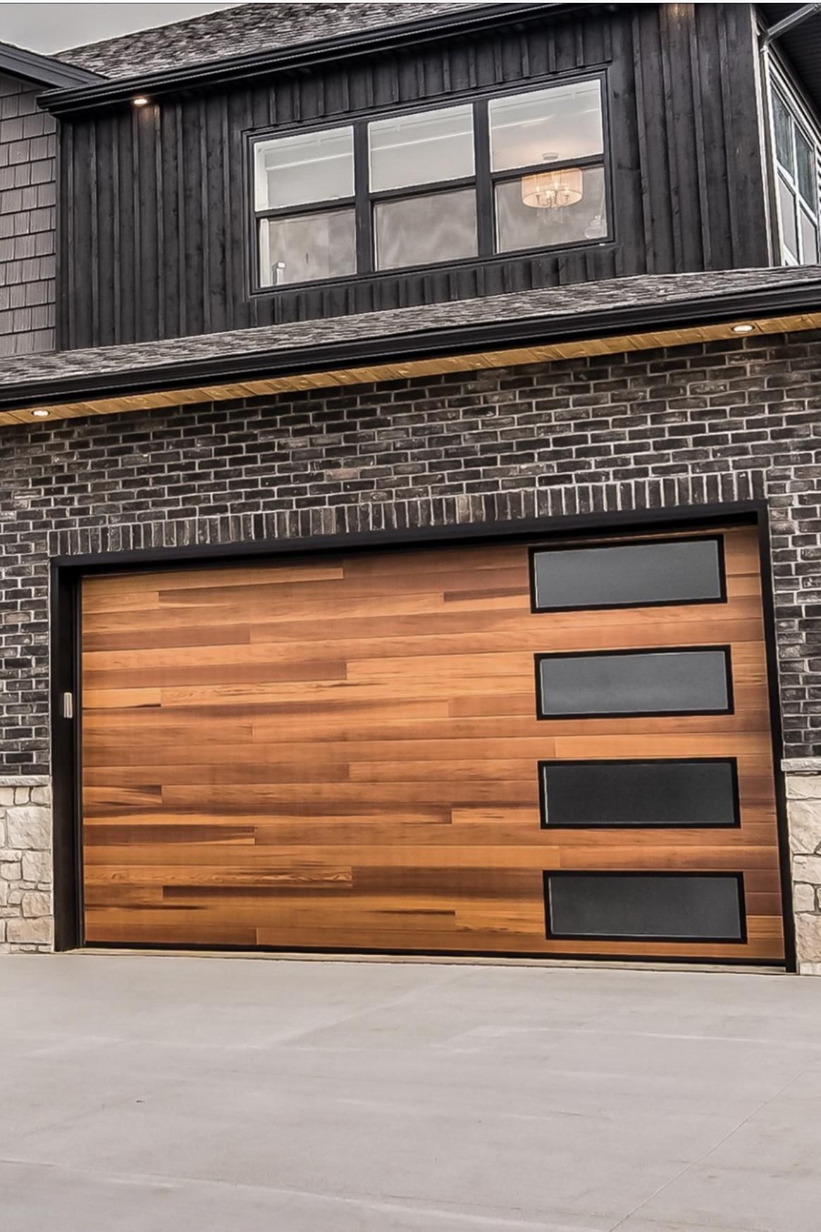 A wooden garage door is sitting in front of a brick house.