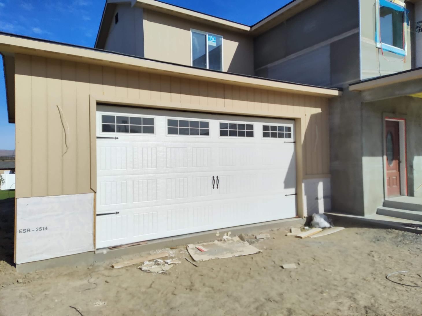 A white garage door is sitting in front of a house under construction.
