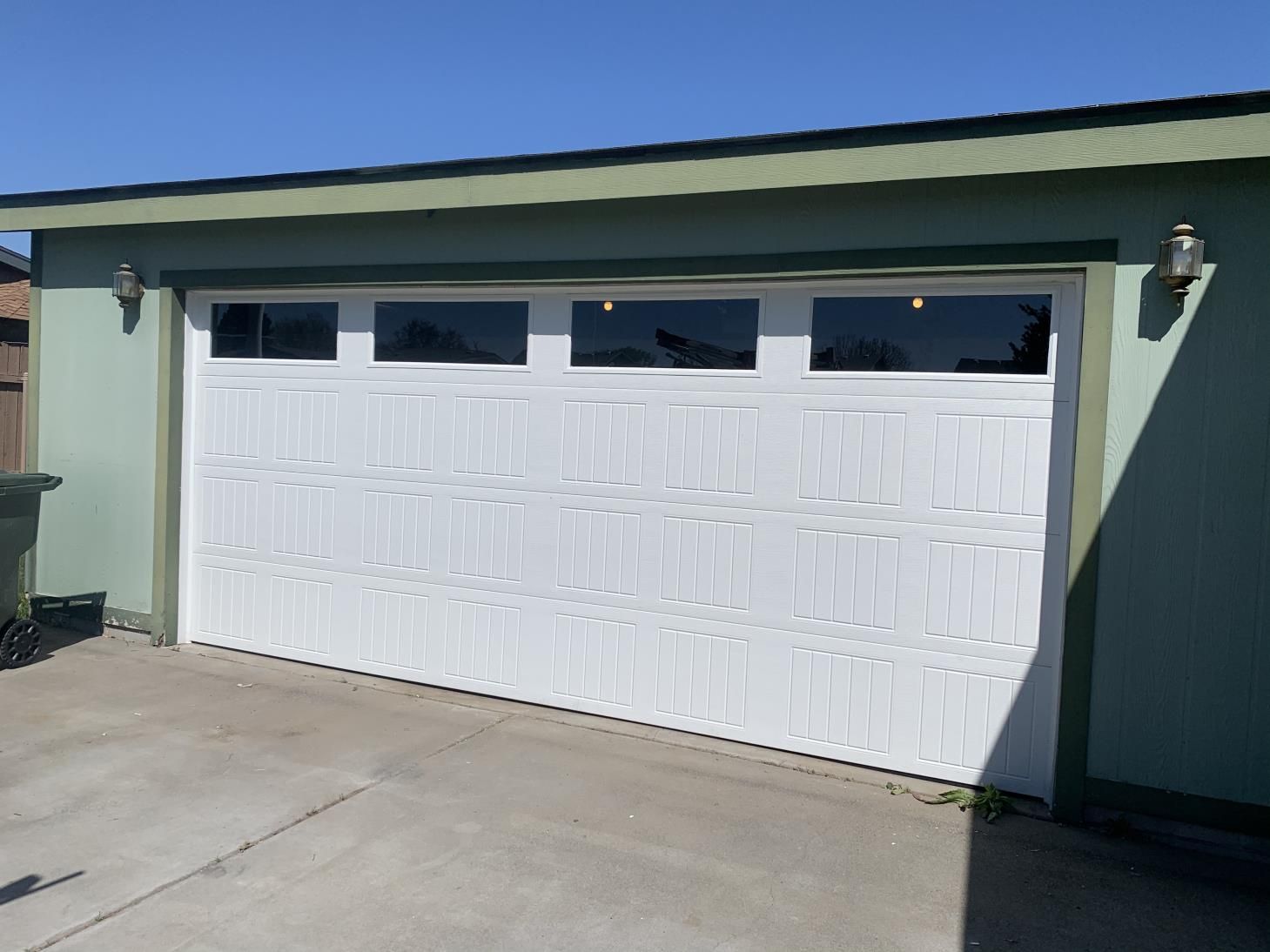A white garage door with a green wall and a blue sky in the background.