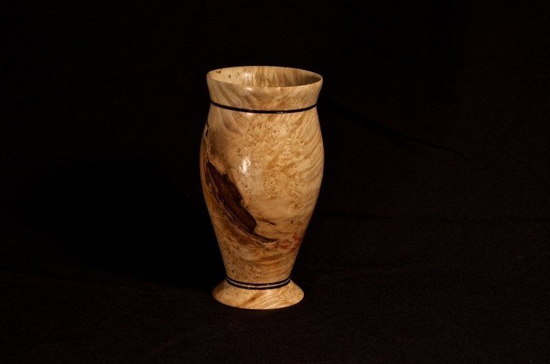 A wooden vase is sitting on a black table.