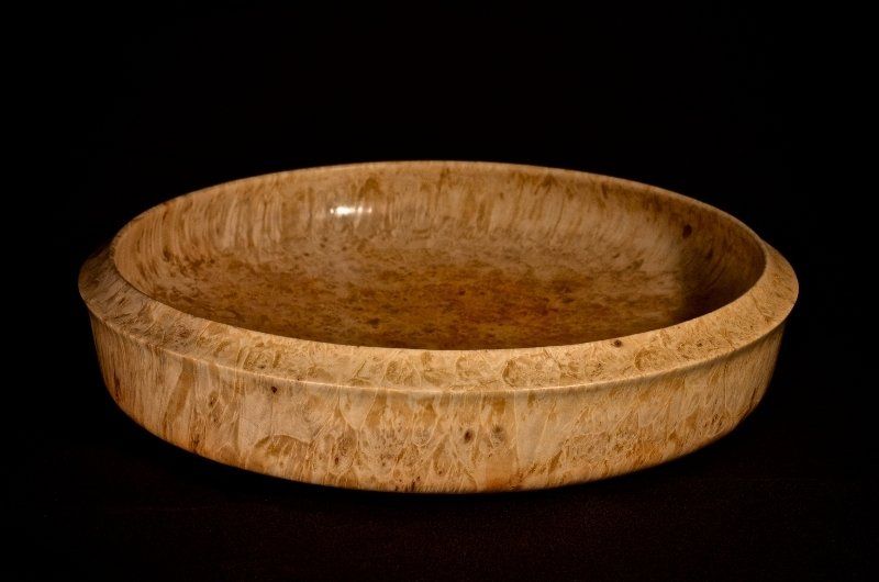 A wooden bowl is sitting on a black surface.