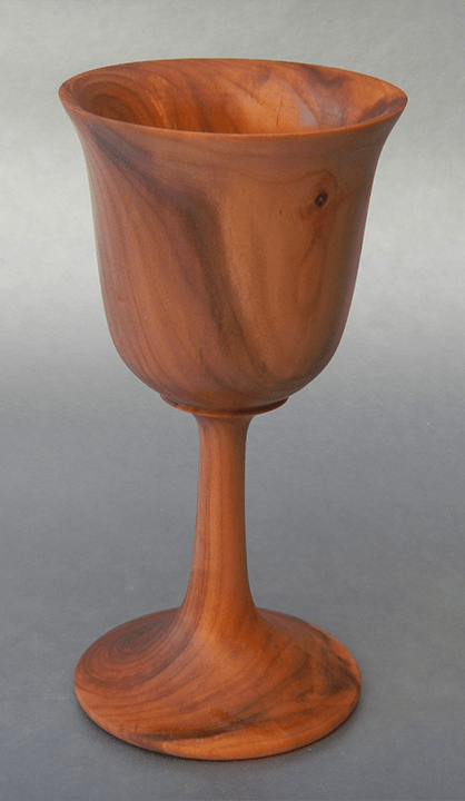 A wooden wine goblet is sitting on a gray surface.