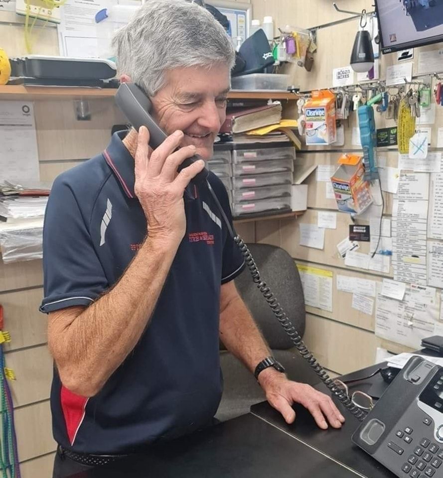 A Man In A Blue Shirt Is Talking On A Phone — Camden Haven Tyre & Brake Centre In Laurieton, NSW