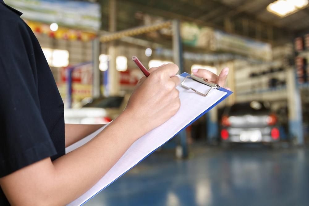 A Woman Is Writing On A Clipboard In A Garage — Camden Haven Tyre & Brake Centre In Laurieton, NSW
