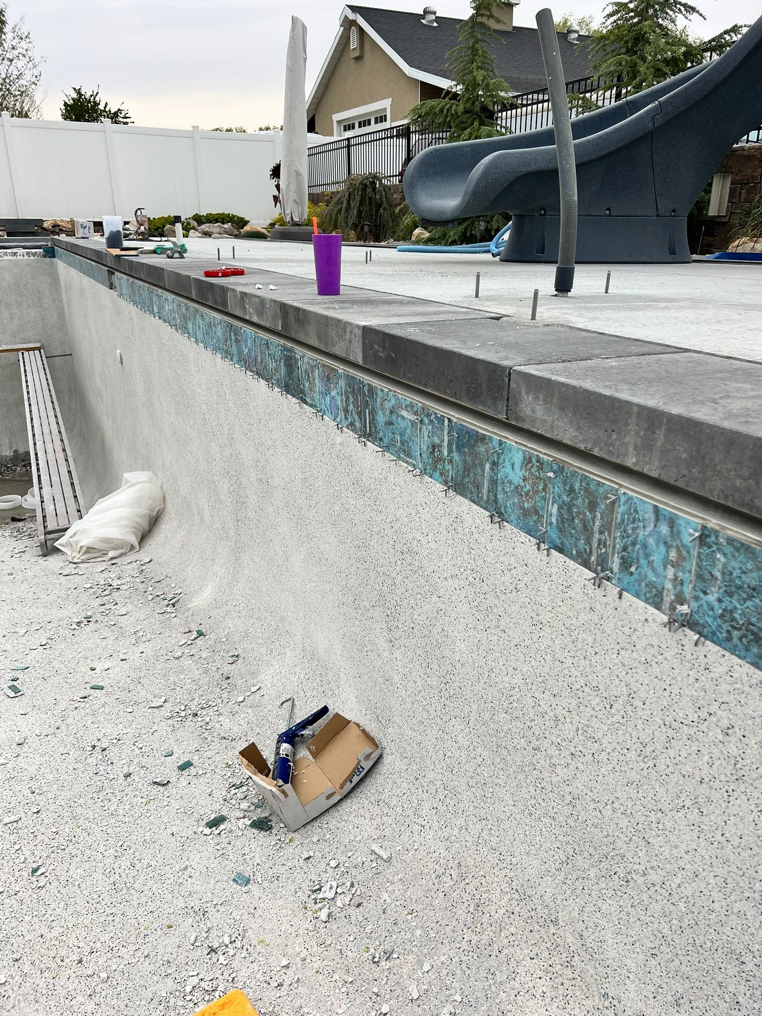 A view of a pool under renovation with a new grey stone coping, blue tile trim, and a freshly applied speckled finish.
